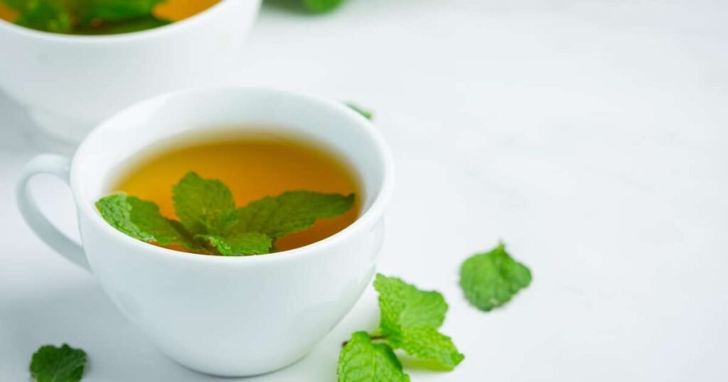 Uma xícara de chá de hortelã fresco, cercada por folhas de hortelã e limão, simbolizando os benefícios à saúde.
