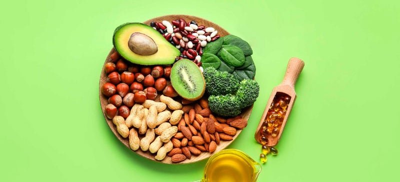 Variedade de alimentos ricos em vitamina E, incluindo óleo de gérmen de trigo, sementes de girassol, amêndoas, e abacate.
