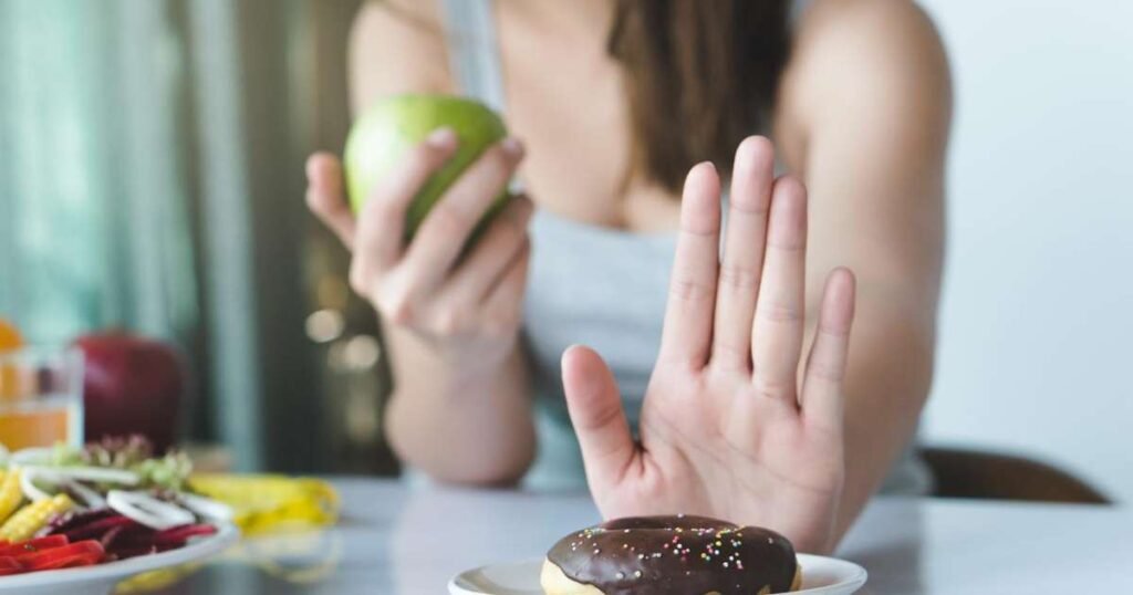 Uma pessoa segurando uma maçã e ignorando um doce, simbolizando a redução do açúcar na dieta.